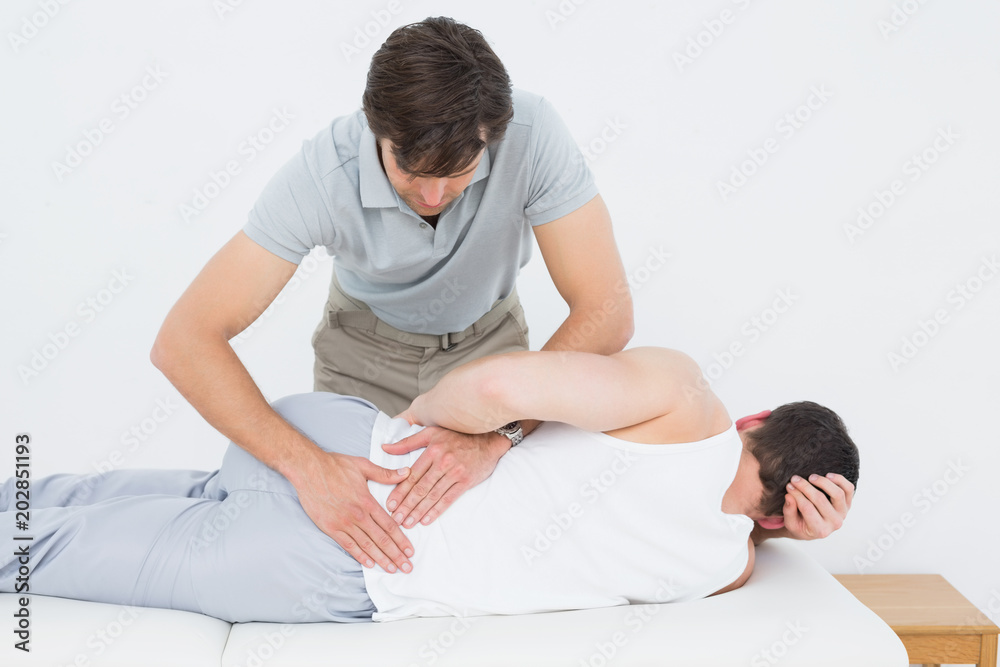 Male physiotherapist examining mans back Male physiotherapist examining mans back