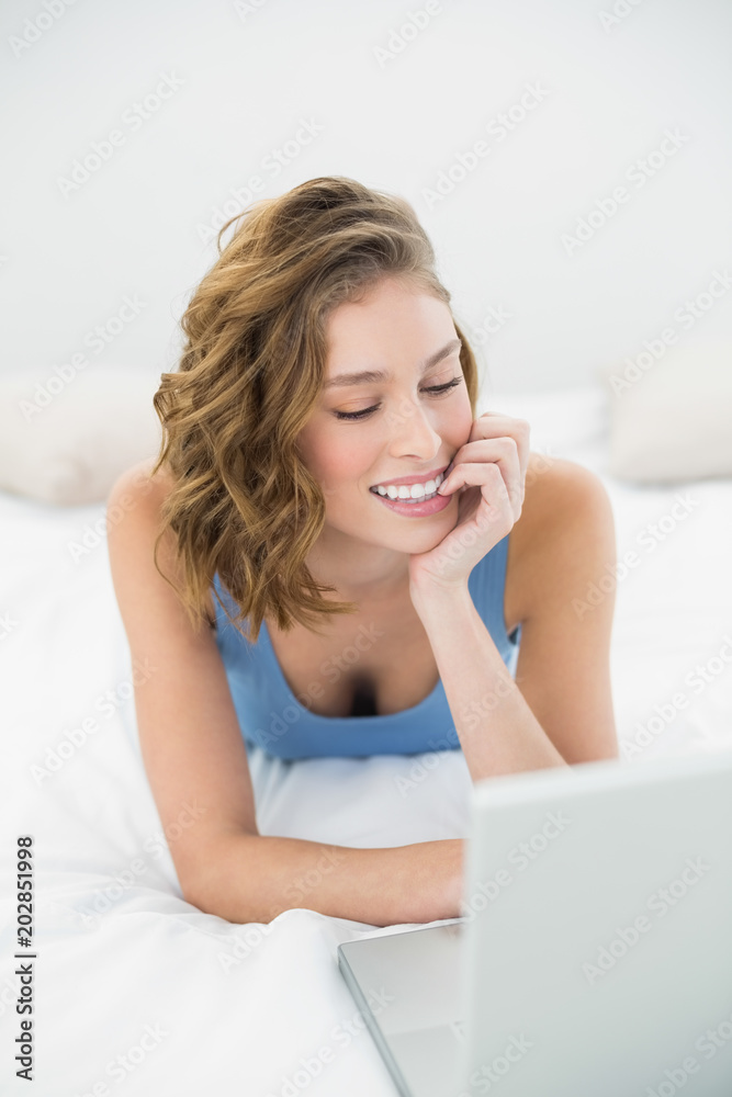Peaceful young woman working with her notebook lying on her bed Peaceful young woman working with her notebook lying on her bed