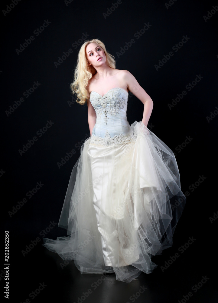 full length portrait of woman wearing white bridal gown. standing poison black studio background.