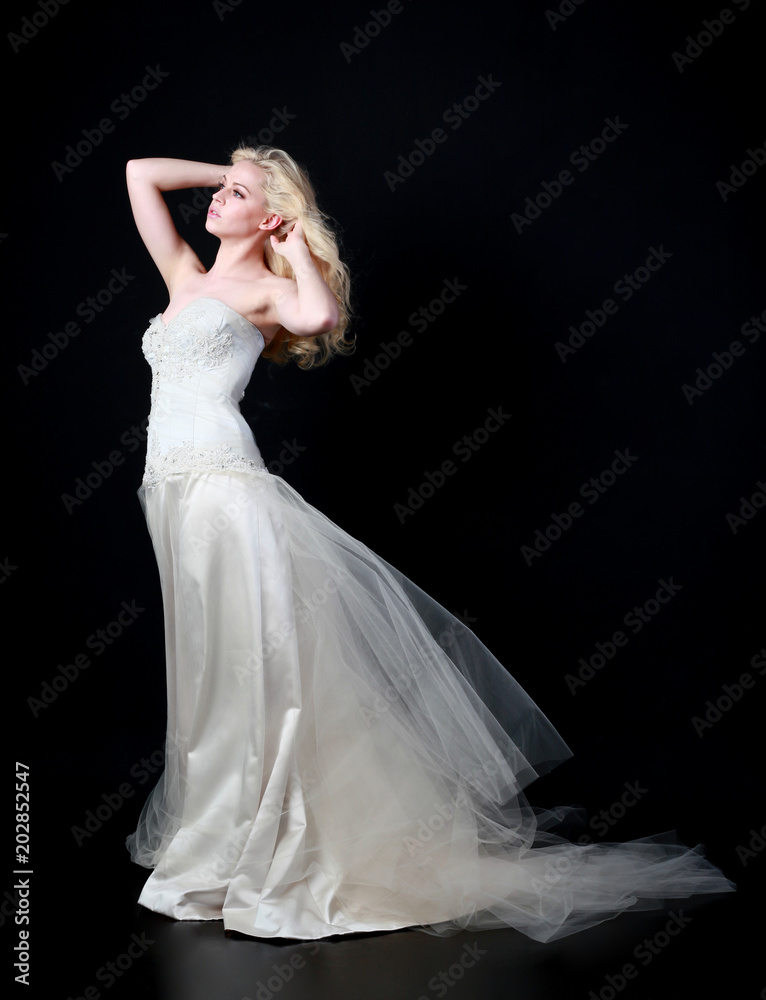 Fototapeta premium full length portrait of woman wearing white bridal gown. standing poison black studio background.