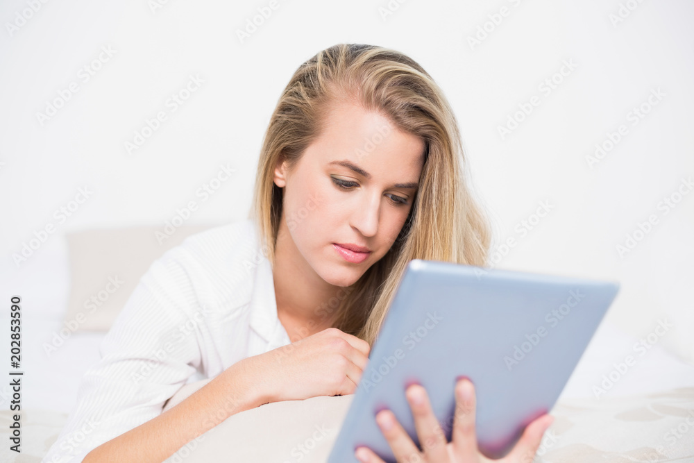 Focused pretty model using her tablet pc lying on cosy bed Focused pretty model using her tablet pc lying on cosy bed