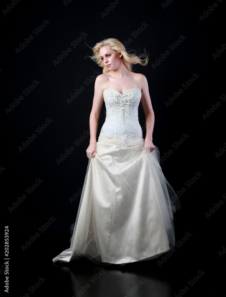 full length portrait of woman wearing white bridal gown. standing poison black studio background.