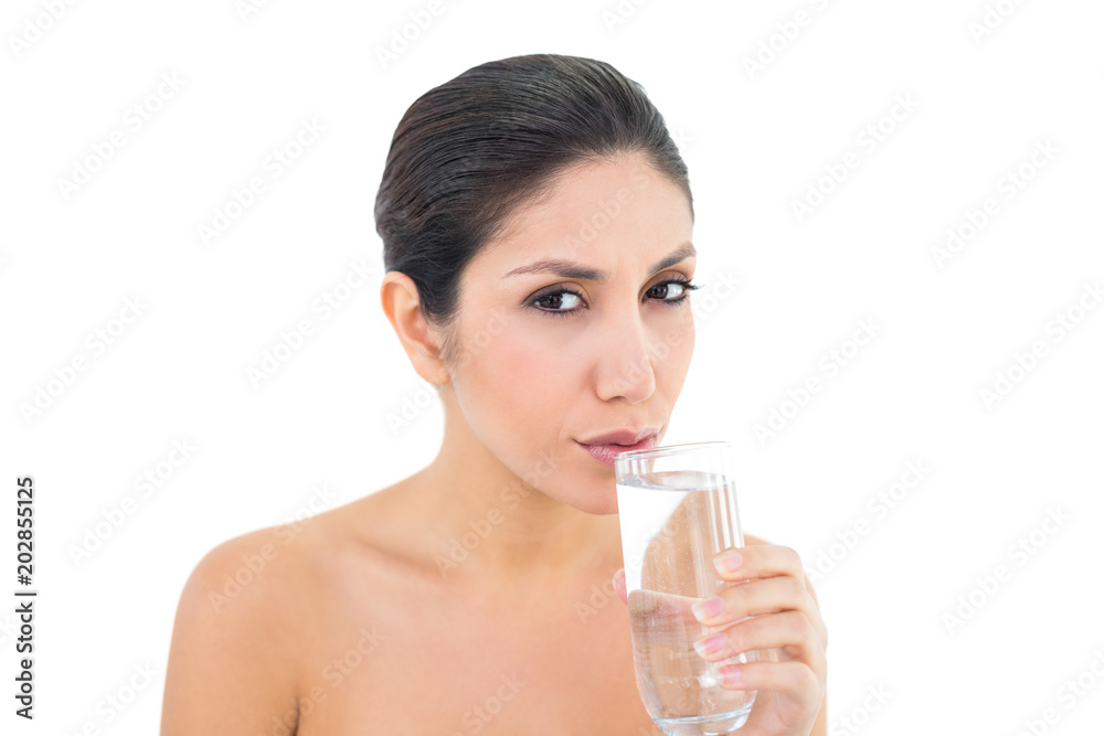 Happy brunette sipping glass of water and looking at camera Happy brunette sipping glass of water and looking at camera