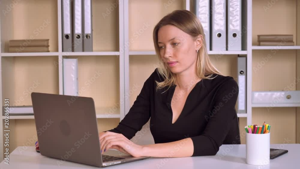 adult business woman working in modern office. beautiful caucasian employer working with computer looking on screen laptop with happy smile. attractive worker with blonde hair wearing elegant black adult business woman working in modern office. beautiful caucasian employer working with computer looking on screen laptop with happy smile. attractive worker with blonde hair wearing elegant black
