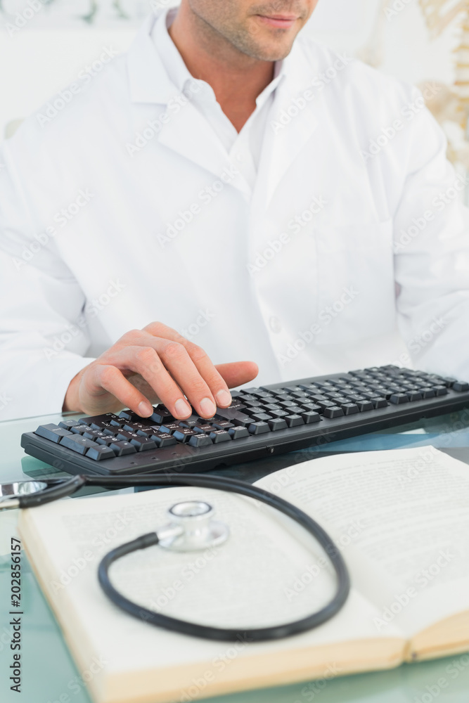 Mid section of a male doctor using computer Mid section of a male doctor using computer