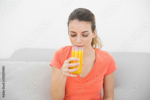 Lovely woman drinking a glass of orange juice sitting on couch