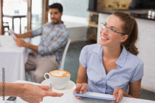 Woman receiving coffee while using digital tablet in coffee shop