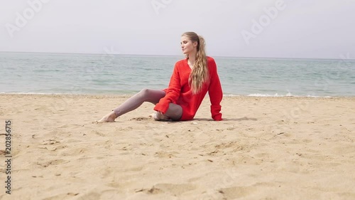 blonde girl is sitting on the sand by the sea and posing for a photo shoot photo