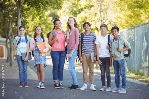 Portrait of happy students standing with books on road