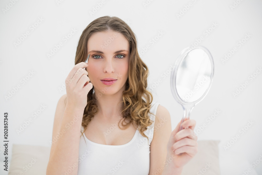Pretty woman plucking her eyebrows while looking into the camera Pretty woman plucking her eyebrows while looking into the camera