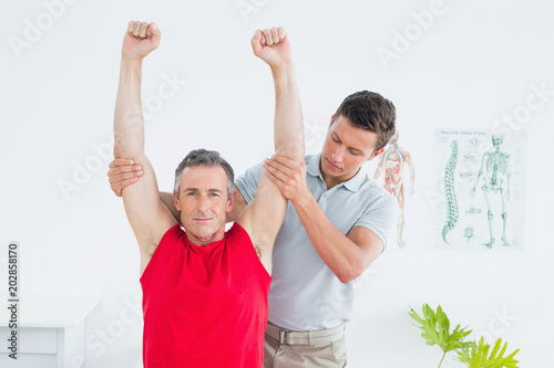 Physiotherapist stretching a mature mans arms