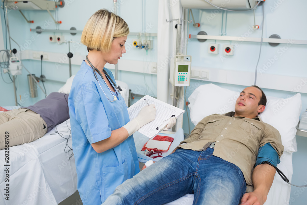 Nurse writing on a clipboard next to transfused patients Nurse writing on a clipboard next to transfused patients