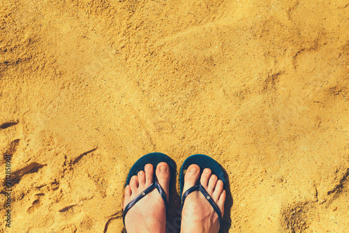 Φωτογραφία Woman legs in slippers on yellow sand background