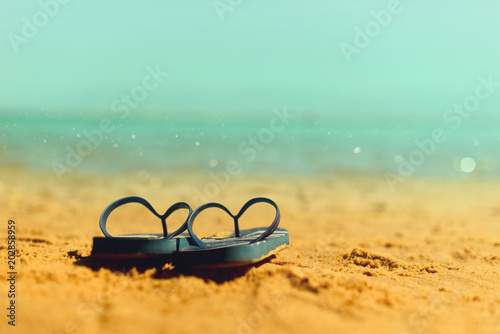 Navy flip flop on yellow sand beach with blue sea and sky background. Copy space. Summer, holiday and travel concept