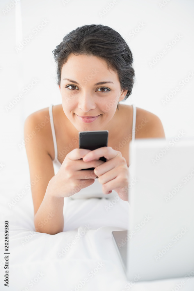 Relaxed casual brunette in white pajamas using her mobile phone