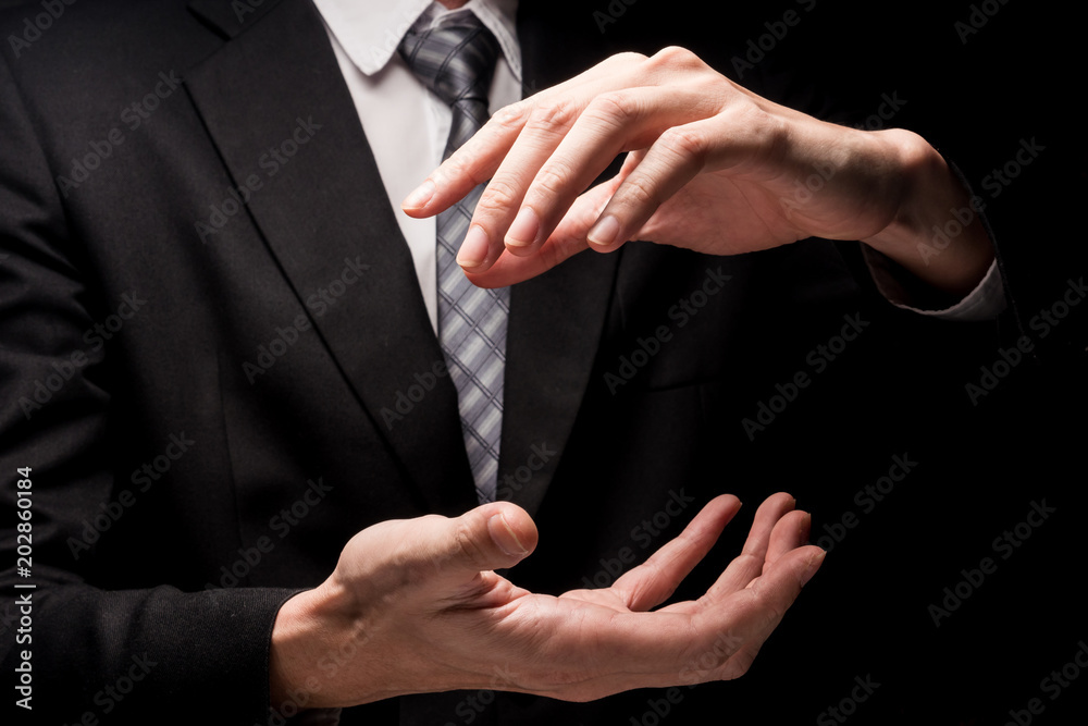 Obraz premium Close up of man in black suit with hand gesture on black background.