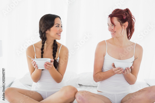 Smiling young female friends with bowls sitting on bed © WavebreakmediaMicro