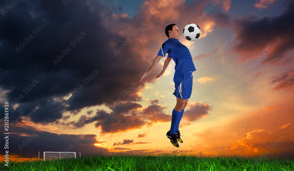 Football player in blue jumping against green grass under blue sky