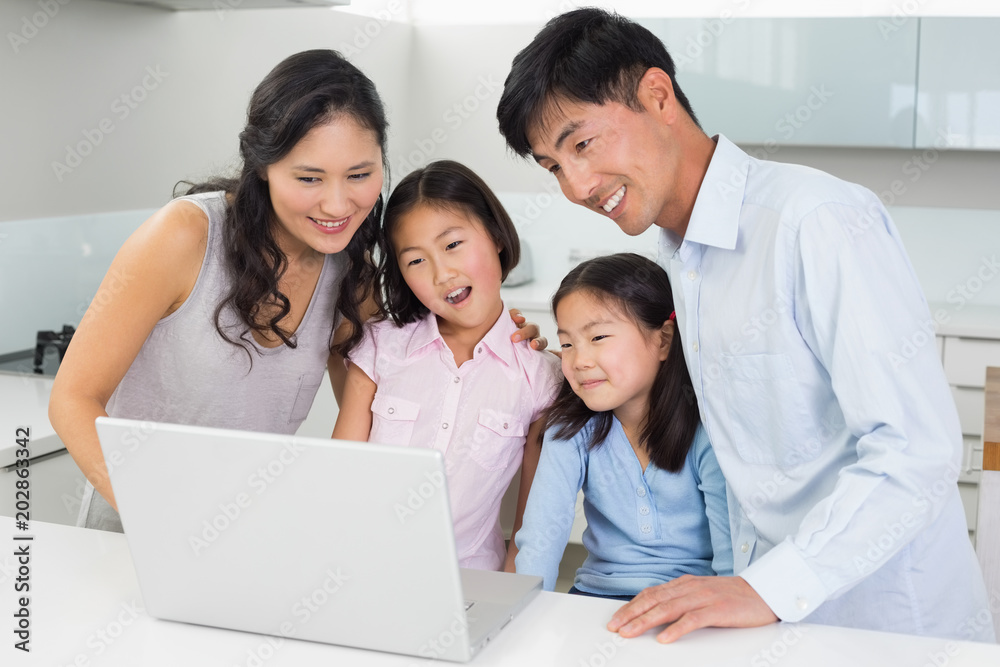 Happy family of four using laptop in kitchen Happy family of four using laptop in kitchen