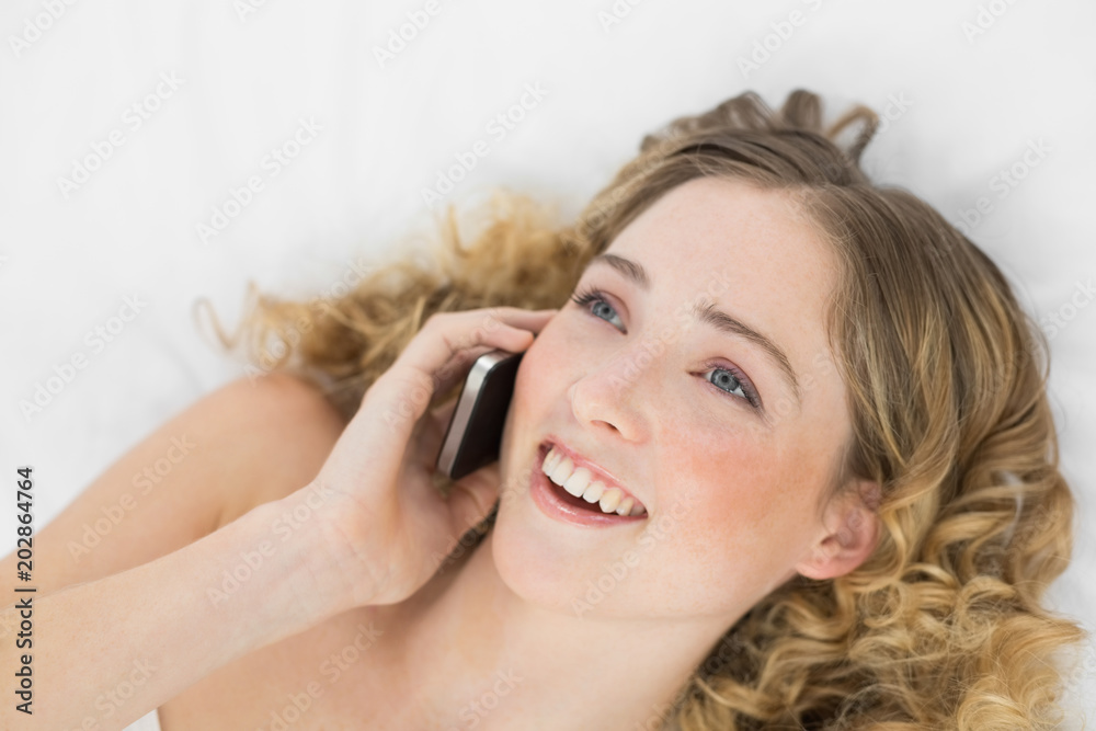 Pretty happy blonde lying on bed phoning with mobile phone Pretty happy blonde lying on bed phoning with mobile phone