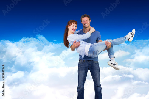 Man lifting up his girlfriend against bright blue sky over clouds