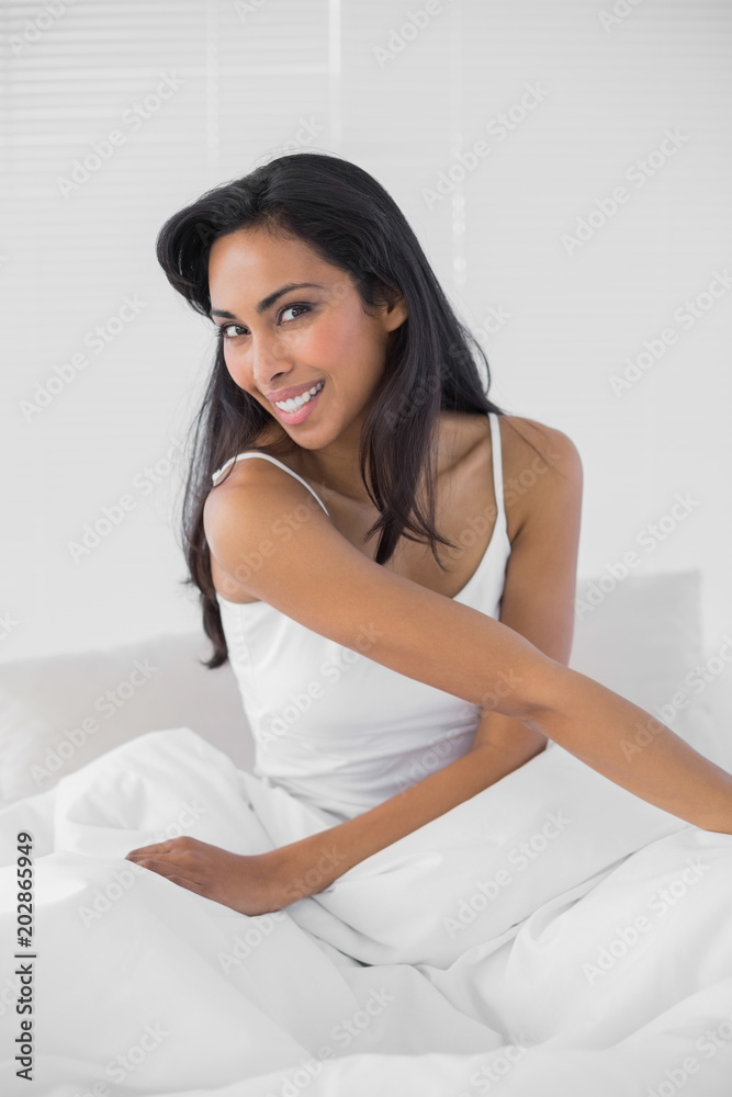 Cute woman smiling cheerfully at camera sitting on her bed Cute woman smiling cheerfully at camera sitting on her bed