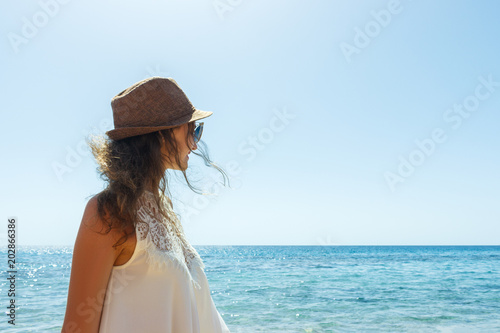 Young woman in hat standing on a beach and looking to a sea horizon