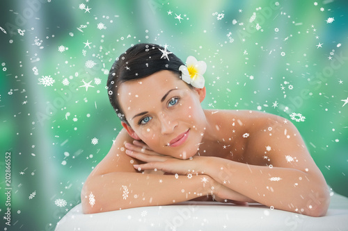 Beautiful brunette relaxing on massage table smiling at camera against snow falling © vectorfusionart