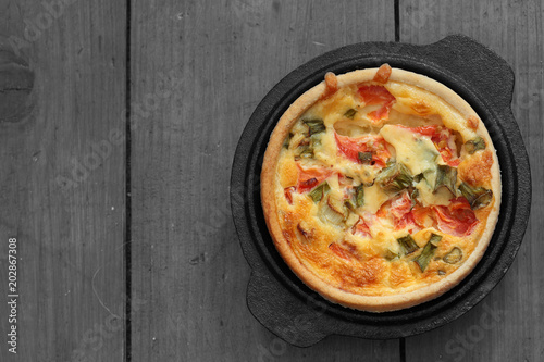 Tomato and spring onion quiche in a cast iron pot dish on a wood background with selective color