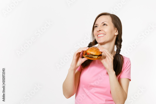 Young beautiful woman in pink t-shirt with braids holding in hands burger isolated on white background. Proper nutrition or American classic fast food. Copy space for advertisement. Advertising area.