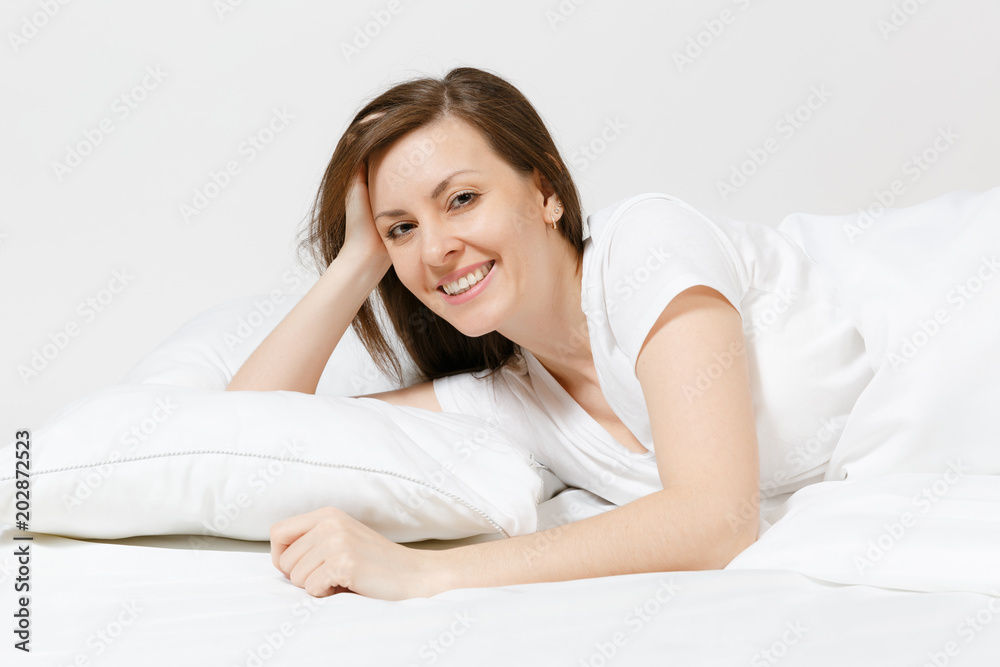 Calm young brunette woman lying in bed with white sheet, pillow, blanket on white background. Smiling beauty female spending time in room. Rest, relax, good mood concept. Copy space for advertisement. Calm young brunette woman lying in bed with white sheet, pillow, blanket on white background. Smiling beauty female spending time in room. Rest, relax, good mood concept. Copy space for advertisement.