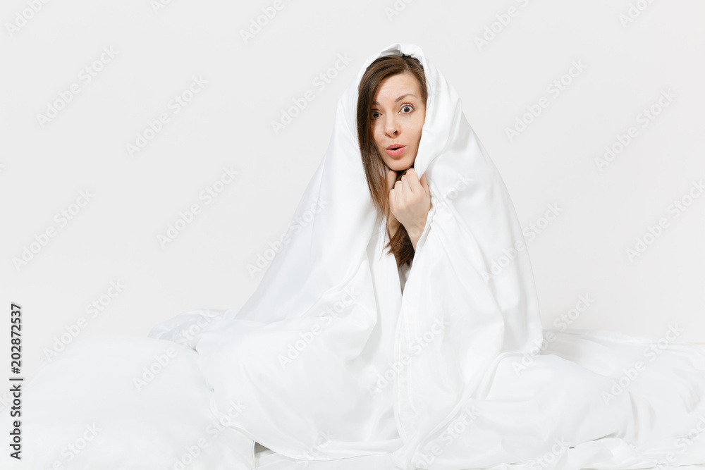 Young brunette woman sitting in bed with white sheet, pillow, wrapping in blanket on white background. Beauty female spending time in room. Rest, relax, good mood concept. Copy space for advertisement Young brunette woman sitting in bed with white sheet, pillow, wrapping in blanket on white background. Beauty female spending time in room. Rest, relax, good mood concept. Copy space for advertisement