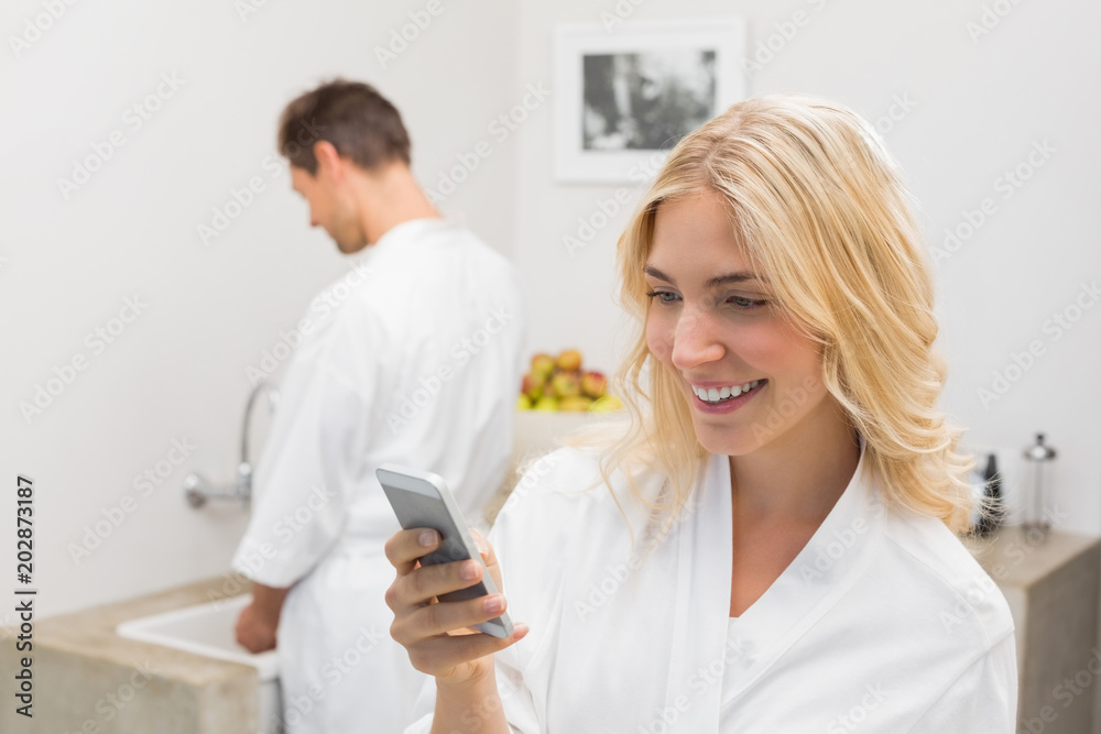 Smiling woman text messaging with man in background at kitchen Smiling woman text messaging with man in background at kitchen