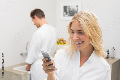 Smiling woman text messaging with man in background at kitchen