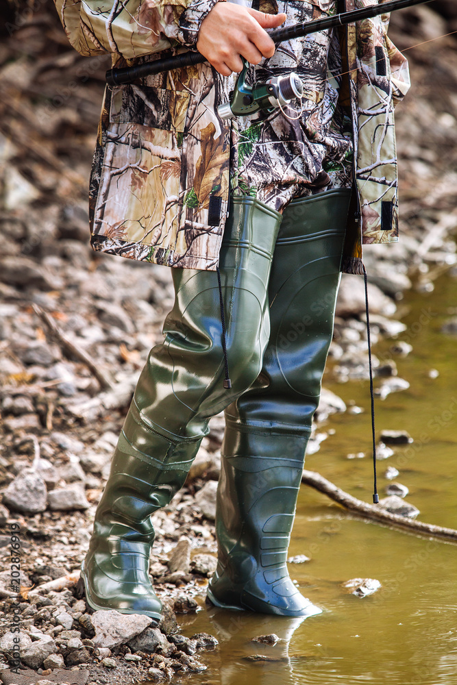 fisherman stands in rubber boots colors of khaki with a fishing rod in his  hands on the river bank Stock Photo | Adobe Stock