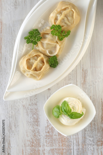 dumpling. Homemade manti dumplings in a white ceramic dish, white sauce with parsley and green basil on light shabby chic background . Manti . Traditional meat dish.