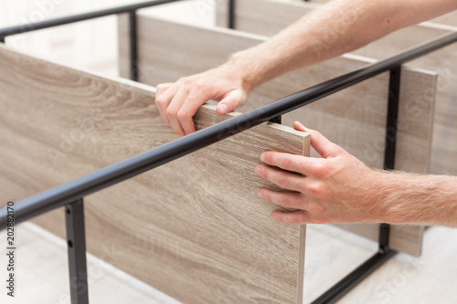 Handyman folds a bookcase. The man is fixing the shelf on the bookshelf.