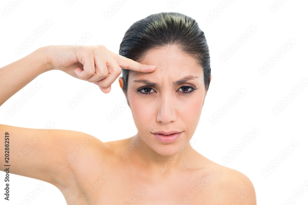 Frowning brunette pointing to forehead and looking at camera