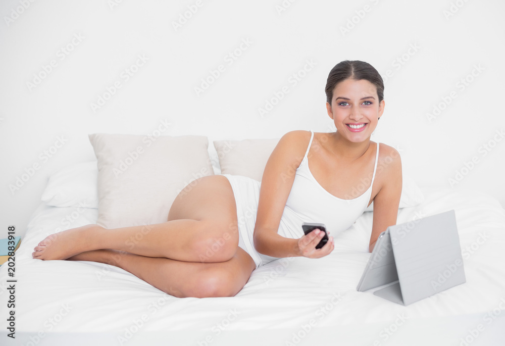 Pretty young brown haired model in white pajamas holding a mobile phone Pretty young brown haired model in white pajamas holding a mobile phone