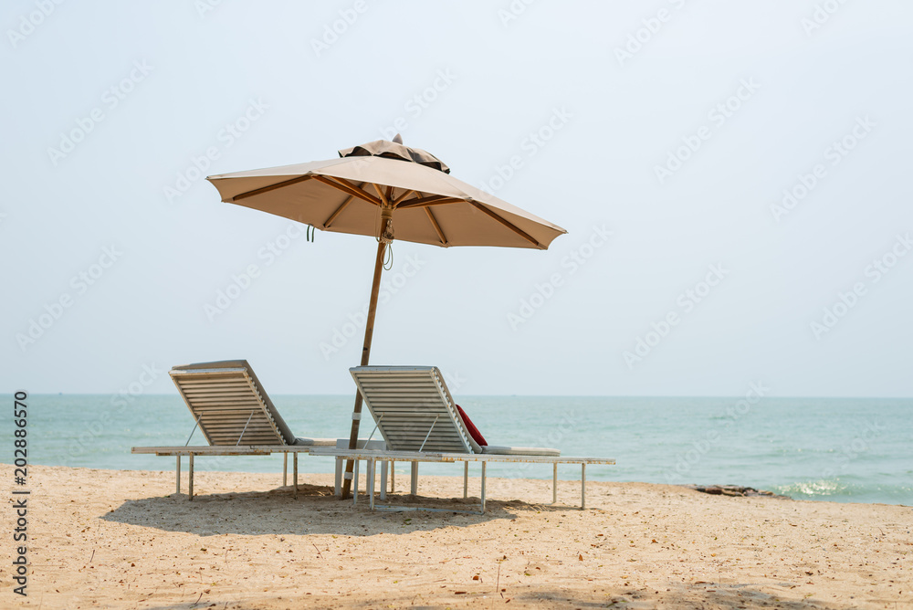 Two sun-beds and umbrella on tropical beach - vacation time