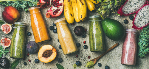 Flat-lay of colorful smoothies in bottles with fresh tropical fruit and superfoods on concrete background, top view. Healthy, vegetarian, detox, dieting breakfast food concept