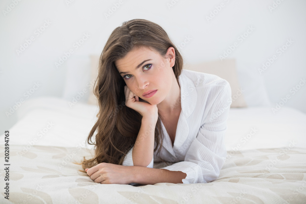 Troubled casual brown haired woman in white pajamas lying on her bed Troubled casual brown haired woman in white pajamas lying on her bed