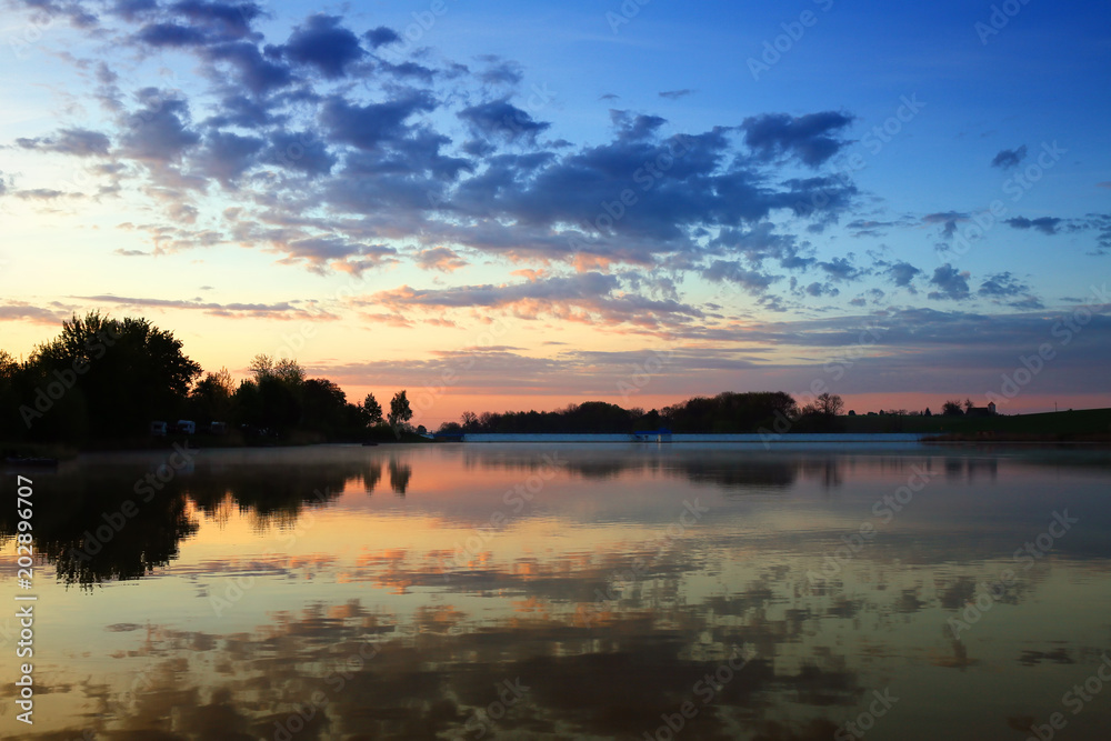 Morning over a lake in Poland, clouds are reflected in the surface of the water 