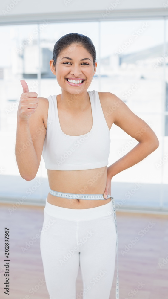 Cheerful woman measuring waist while gesturing thumbs up Cheerful woman measuring waist while gesturing thumbs up