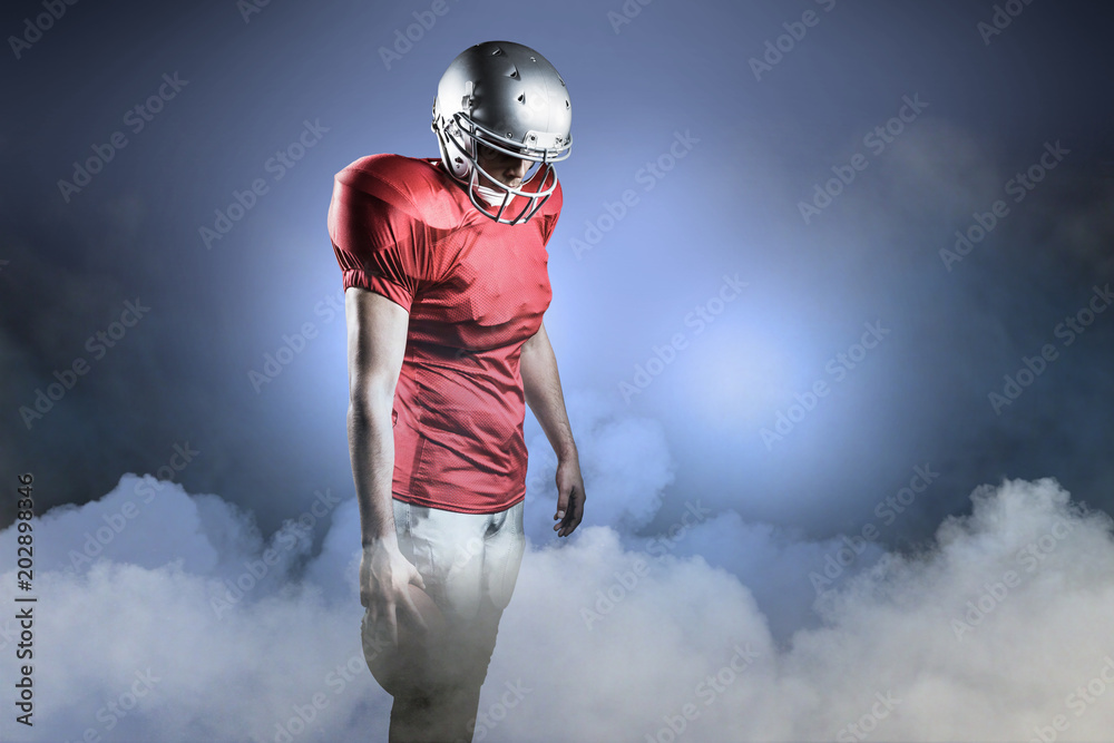 American football player with ball looking down against cloudy sky