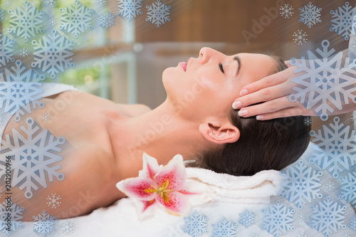 Attractive woman receiving head massage at spa center against snowflake frame