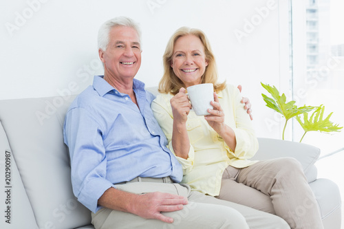 Senior couple with coffee cup sitting on sofa