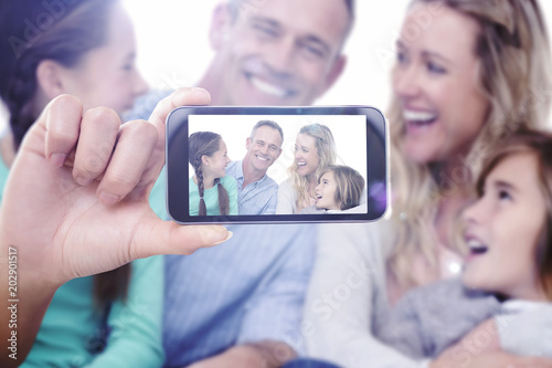 Hand holding smartphone showing against portrait of a smiling family sitting on the floor