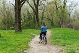 Young girl standing on her bicycle on a dirt road in the forest