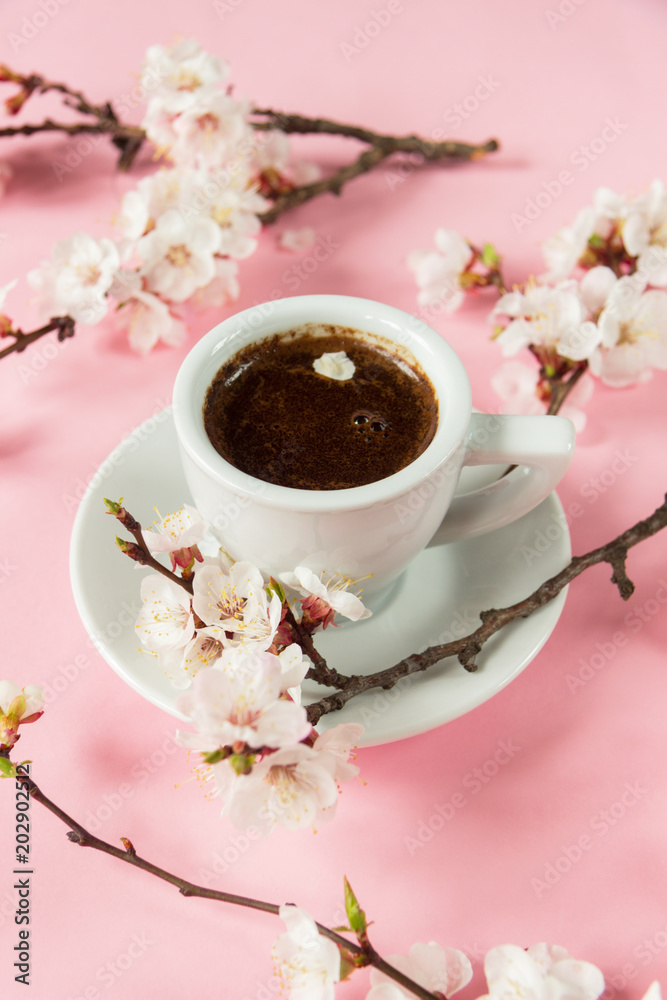 White cup with espresso on pink background with flowering apricot branches. Close-up White cup with espresso on pink background with flowering apricot branches. Close-up